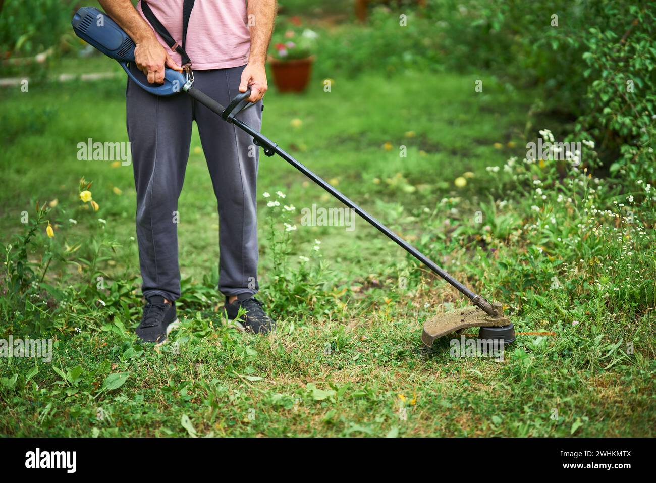 Gros plan d'un jeune homme coupant l'herbe avec un coupe-herbe sur sa pelouse herbeuse. Banque D'Images