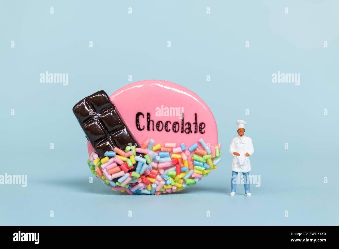 Personnes miniatures, Chef avec biscuit au chocolat sur fond bleu. Concept de la Journée mondiale du chocolat Banque D'Images