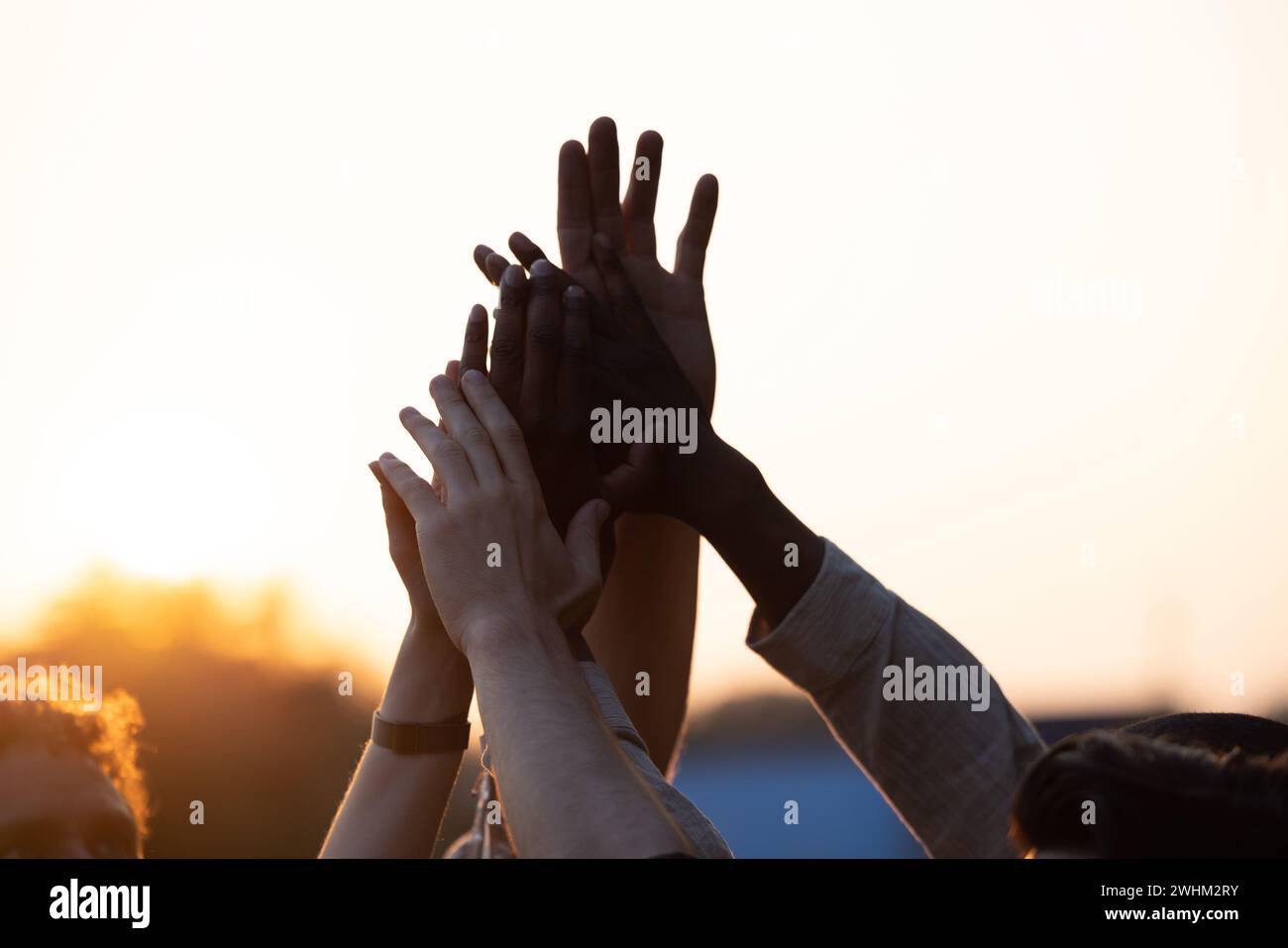 Unity in Silhouette : Multi-racial Friends High-Five et acclamations contre Sunset Sky Banque D'Images