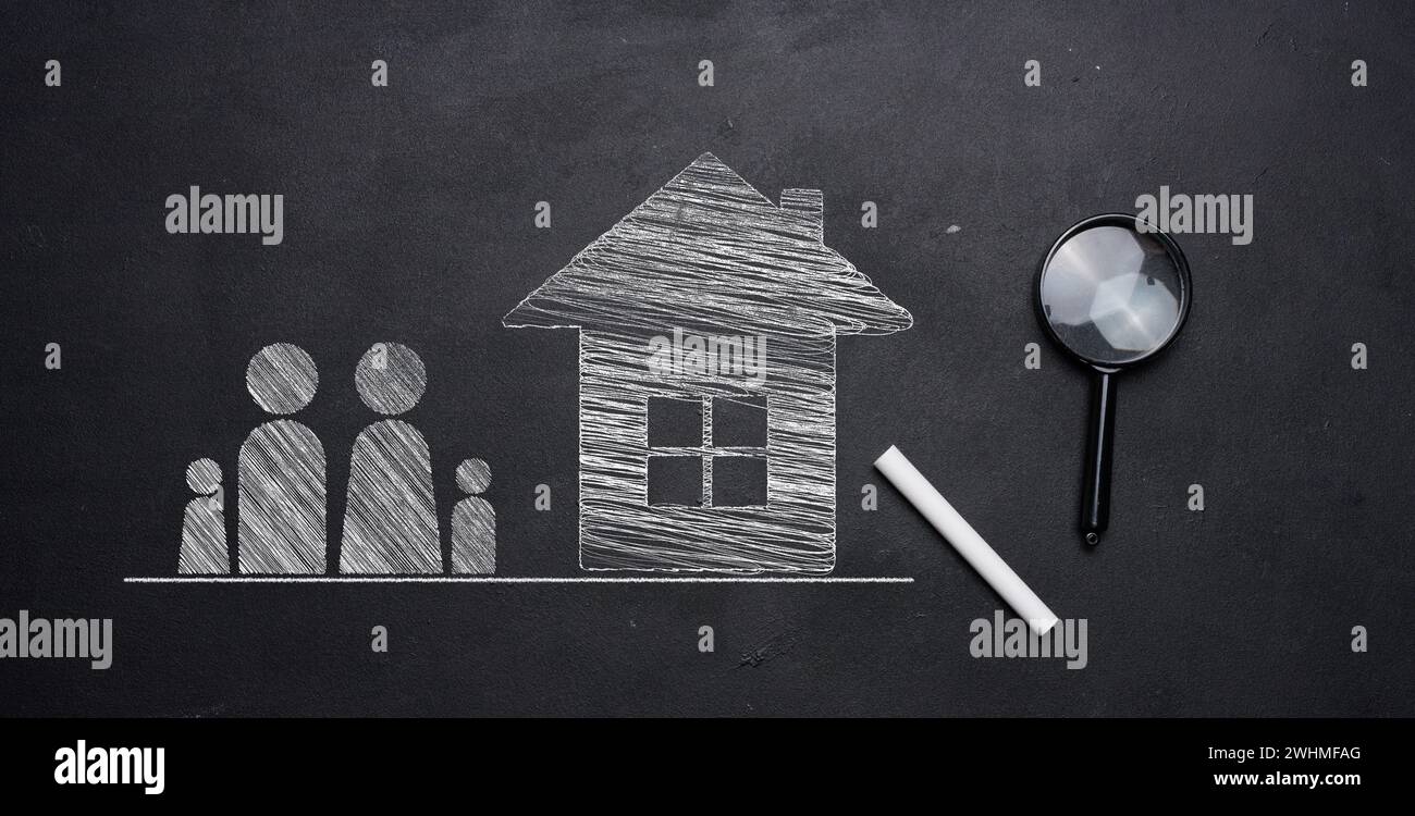 Figures de famille dessinées à la craie et une maison sur un tableau noir, avec une loupe et de la craie à proximité. Concept de mois abordable Banque D'Images