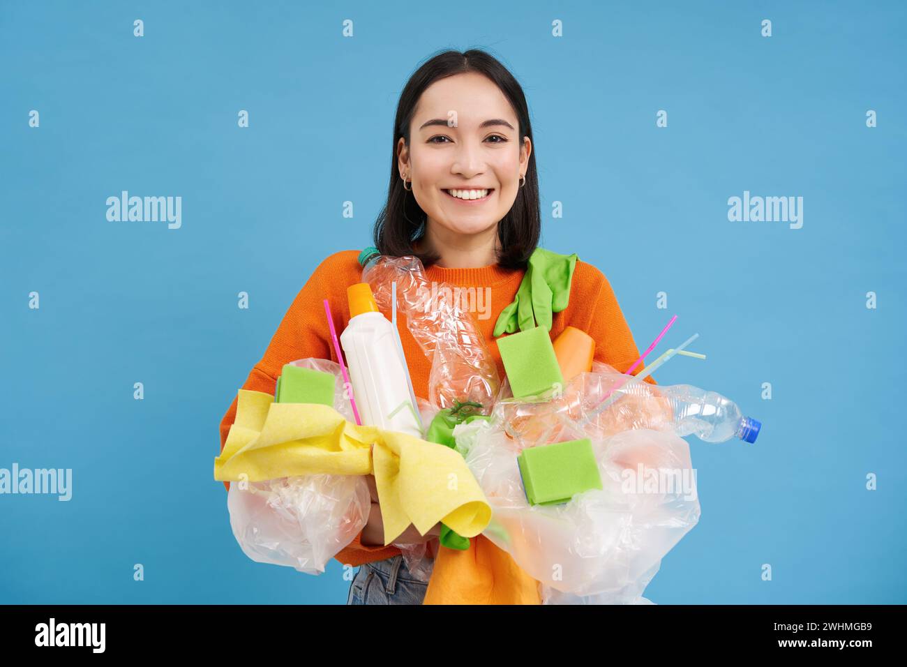 Happy Girl regarde les ordures en plastique, triant ses déchets pour la station de recyclage, souriant excité, fond bleu. Environnement et Banque D'Images