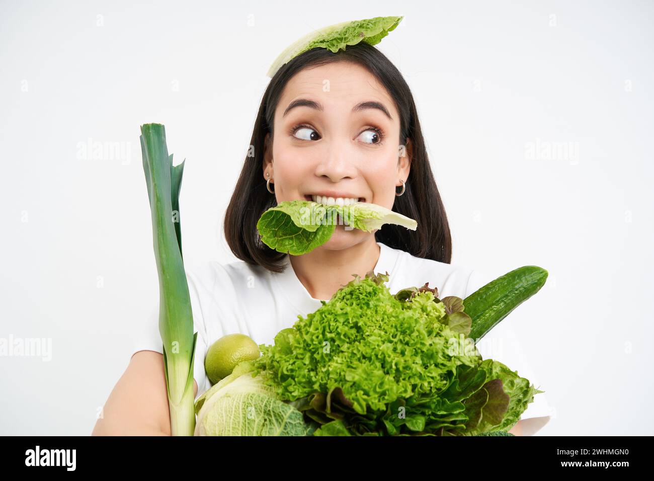 Gros plan portrait d'une fille asiatique grignotant une feuille de laitue, regardant excité, tenant pile de légumes, nourriture biologique verte du gard Banque D'Images