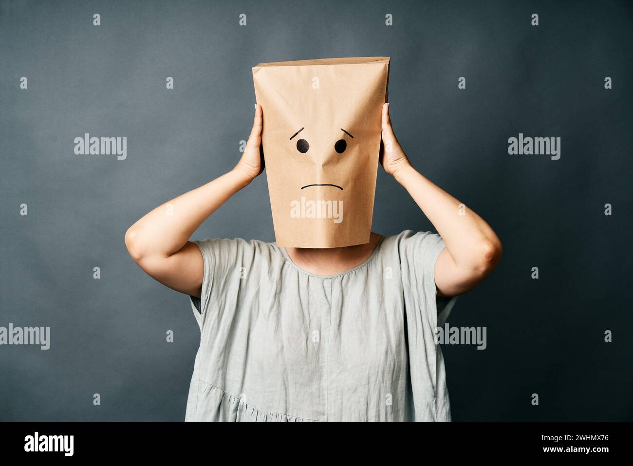 Femme bouleversée avec un sac en papier sur la tête touchant les tempes, souffrant de forts maux de tête de tension Banque D'Images