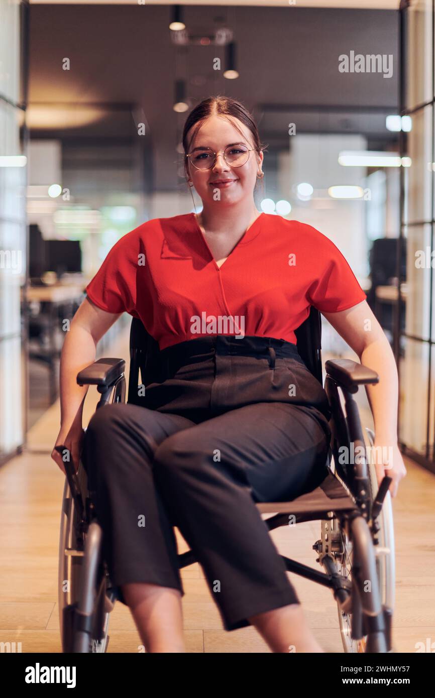 Une jeune femme d'affaires moderne en fauteuil roulant est entourée d'un espace de travail inclusif avec des bureaux vitrés, incarnant determ Banque D'Images