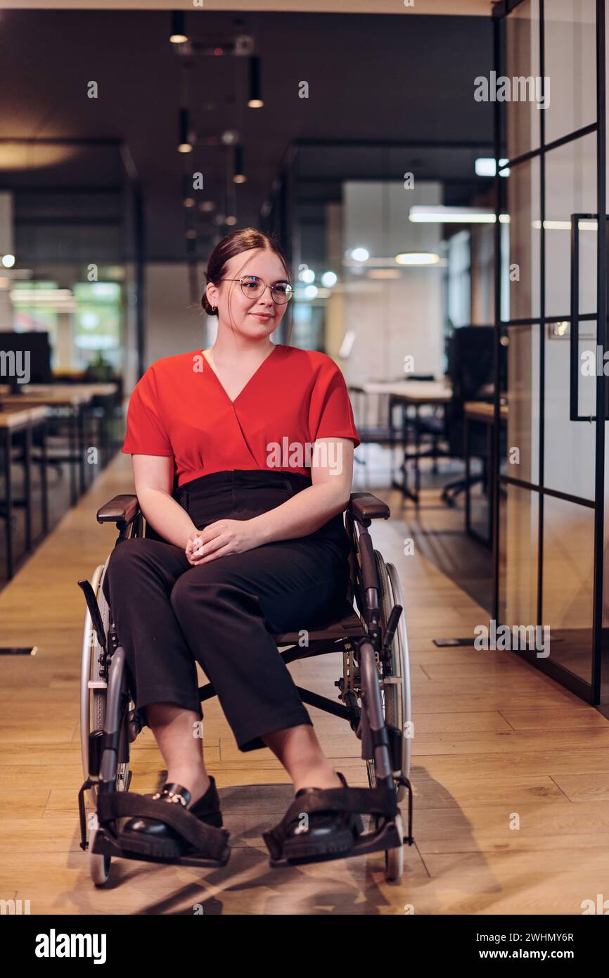 Une jeune femme d'affaires moderne en fauteuil roulant est entourée d'un espace de travail inclusif avec des bureaux vitrés, incarnant determ Banque D'Images