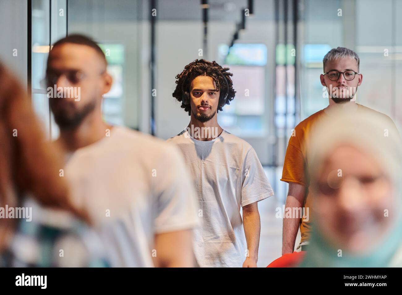 Un groupe diversifié de gens d'affaires marchant un couloir dans le bureau vitré d'une startup moderne, y compris une personne dans un Banque D'Images