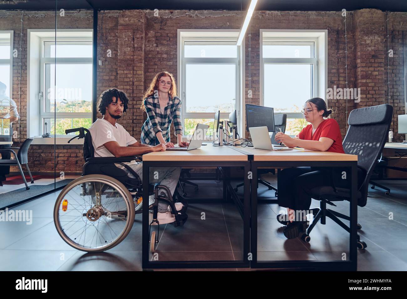 Un jeune groupe d’affaires, dont un homme d’affaires afro-américain en fauteuil roulant, collabore au sein d’un bureau moderne en verre, AC Banque D'Images