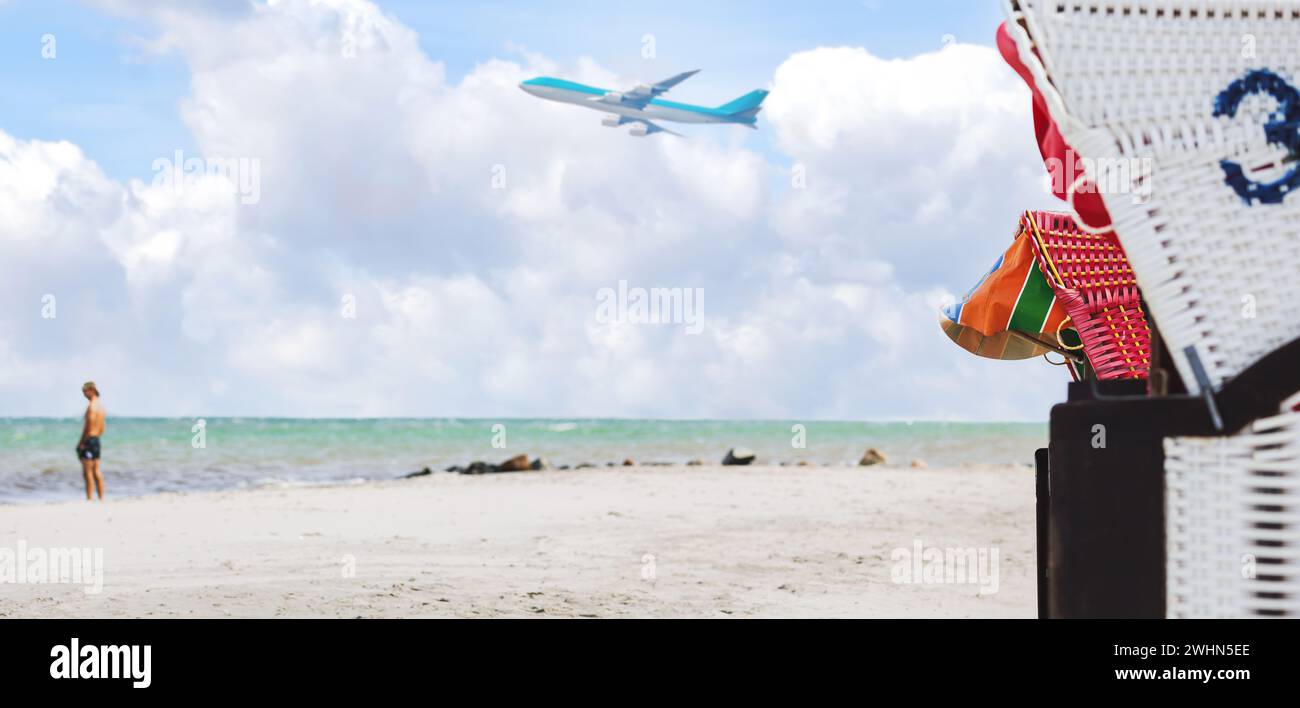 Panorama sur la plage avec chaise de plage en osier. Avion dans le ciel bleu avec des nuages d'en bas Banque D'Images