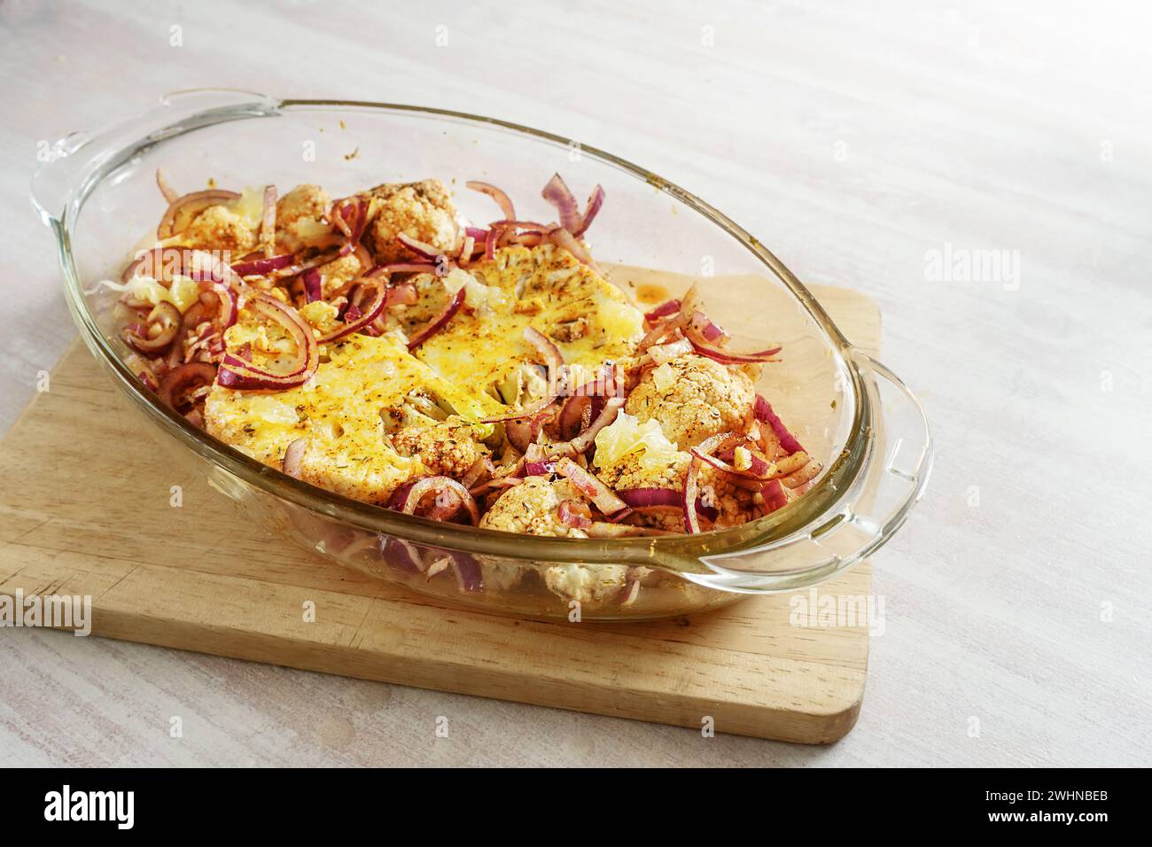 Biftecks de chou-fleur cuits épicés avec des oignons rouges dans une casserole en verre sur une table de cuisine en bois sur une table lumineuse, végétarien veget Banque D'Images