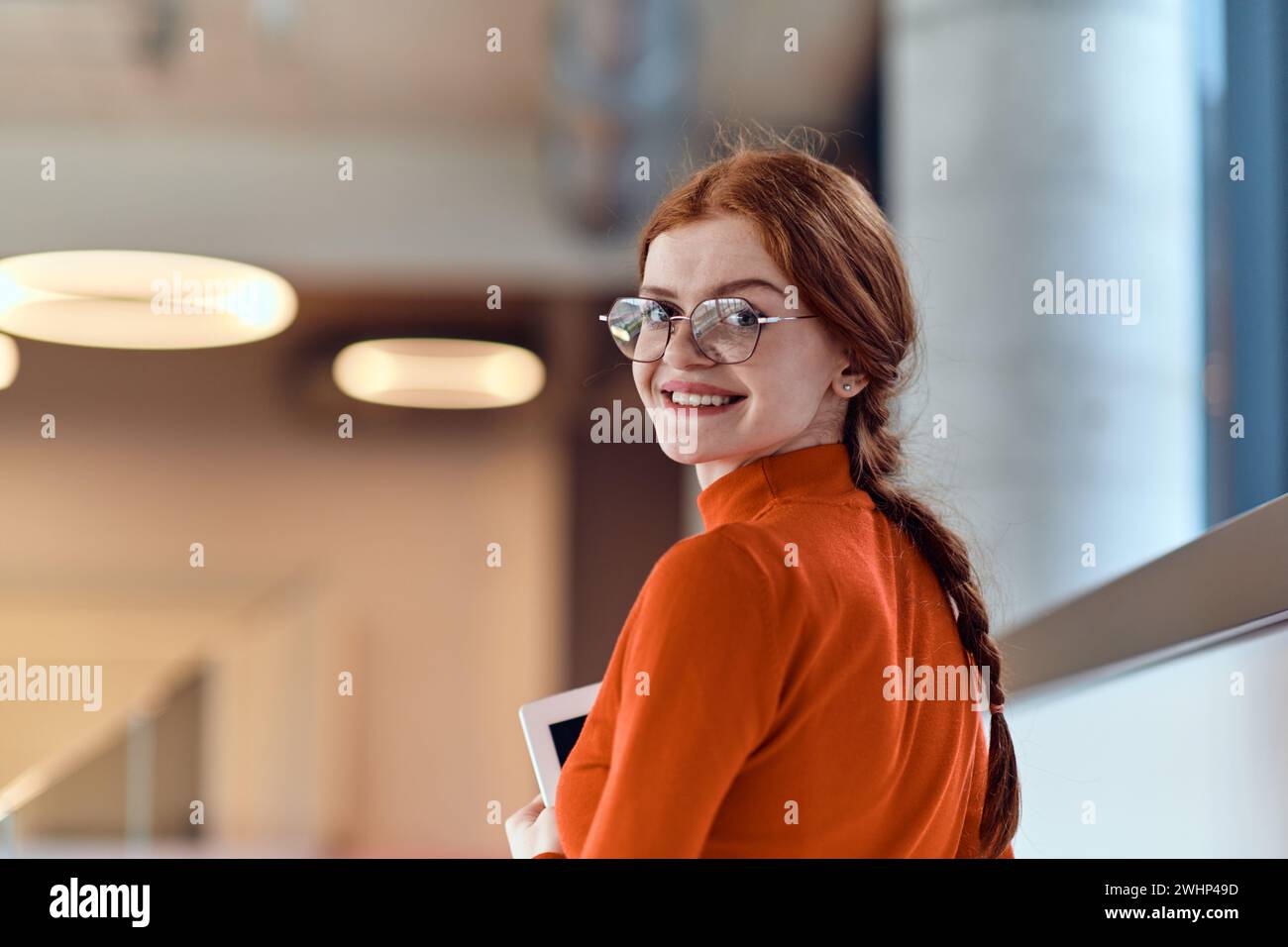 Dans un bureau de start-up moderne dynamique, une femme d'affaires aux cheveux orange frappants est immergée dans son travail à son bureau, incarnant le Banque D'Images