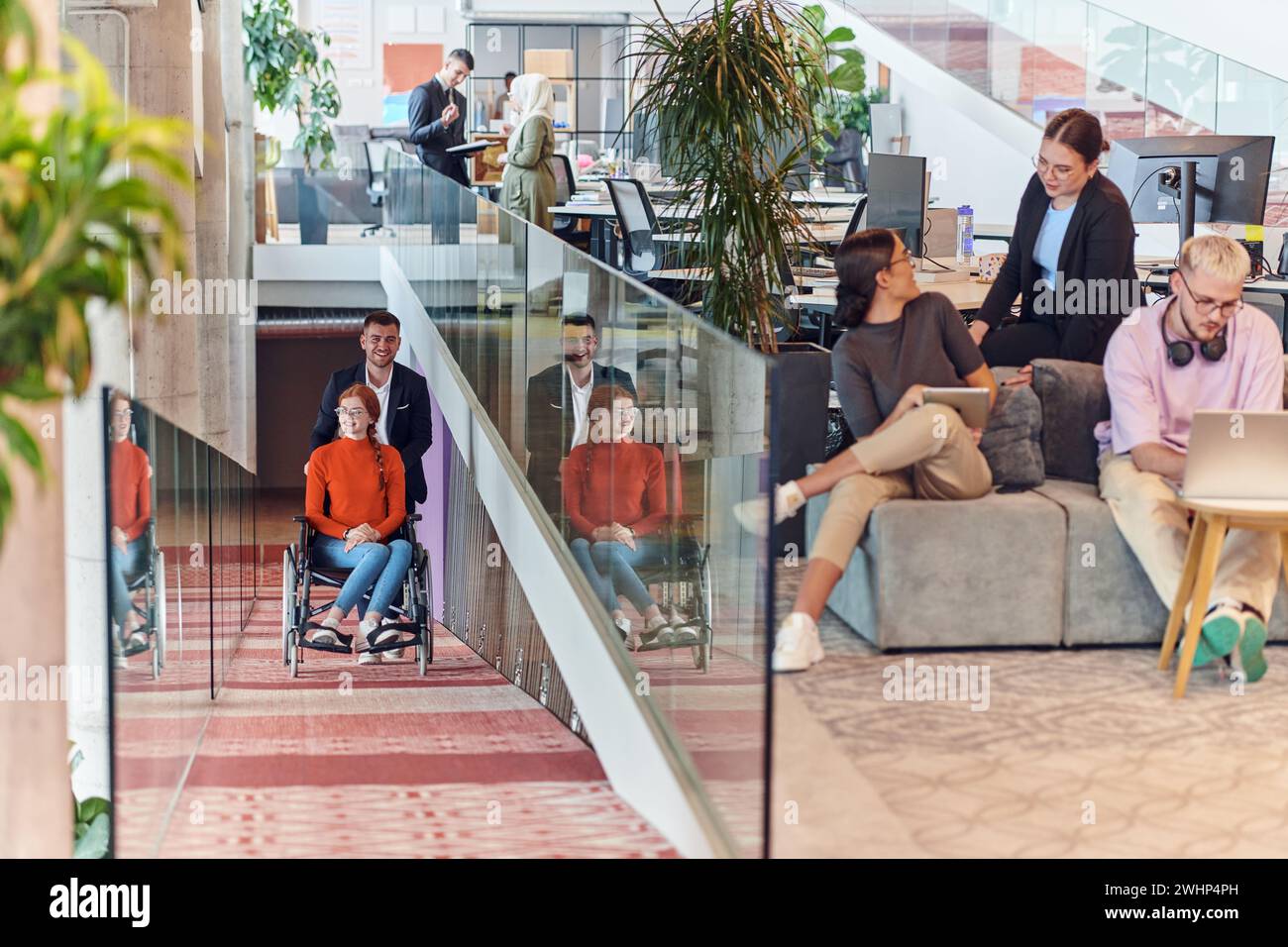 Un directeur d’entreprise assiste son collègue d’affaires en fauteuil roulant, l’aidant à se rendre à son bureau de démarrage, où il travaille Banque D'Images