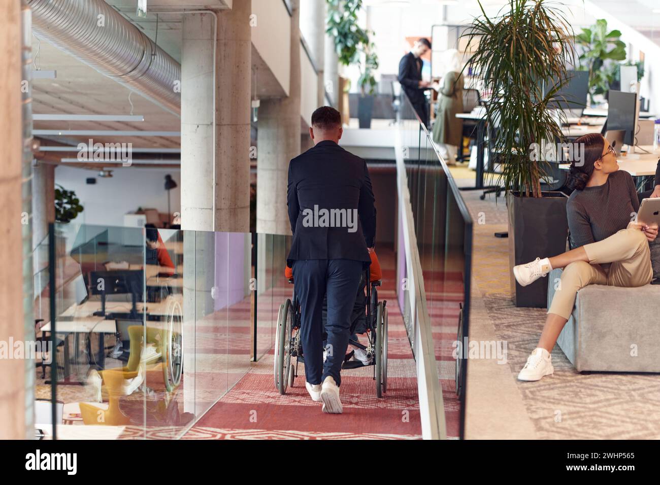 Un directeur d’entreprise assiste son collègue d’affaires en fauteuil roulant, l’aidant à se rendre à son bureau de démarrage, où il travaille Banque D'Images