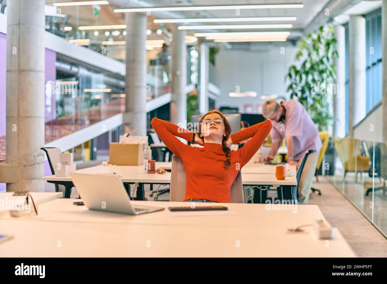 Dans un bureau de démarrage moderne, une femme d'affaires professionnelle avec les cheveux orange assis à son ordinateur portable et reposant sur la pause de travail Banque D'Images