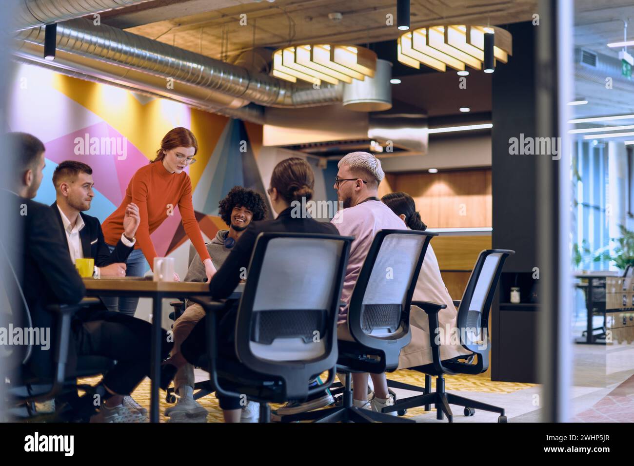 Une équipe diversifiée d'experts en affaires dans un bureau de verre moderne, écoutant attentivement la présentation d'un collègue, encourageant coll Banque D'Images