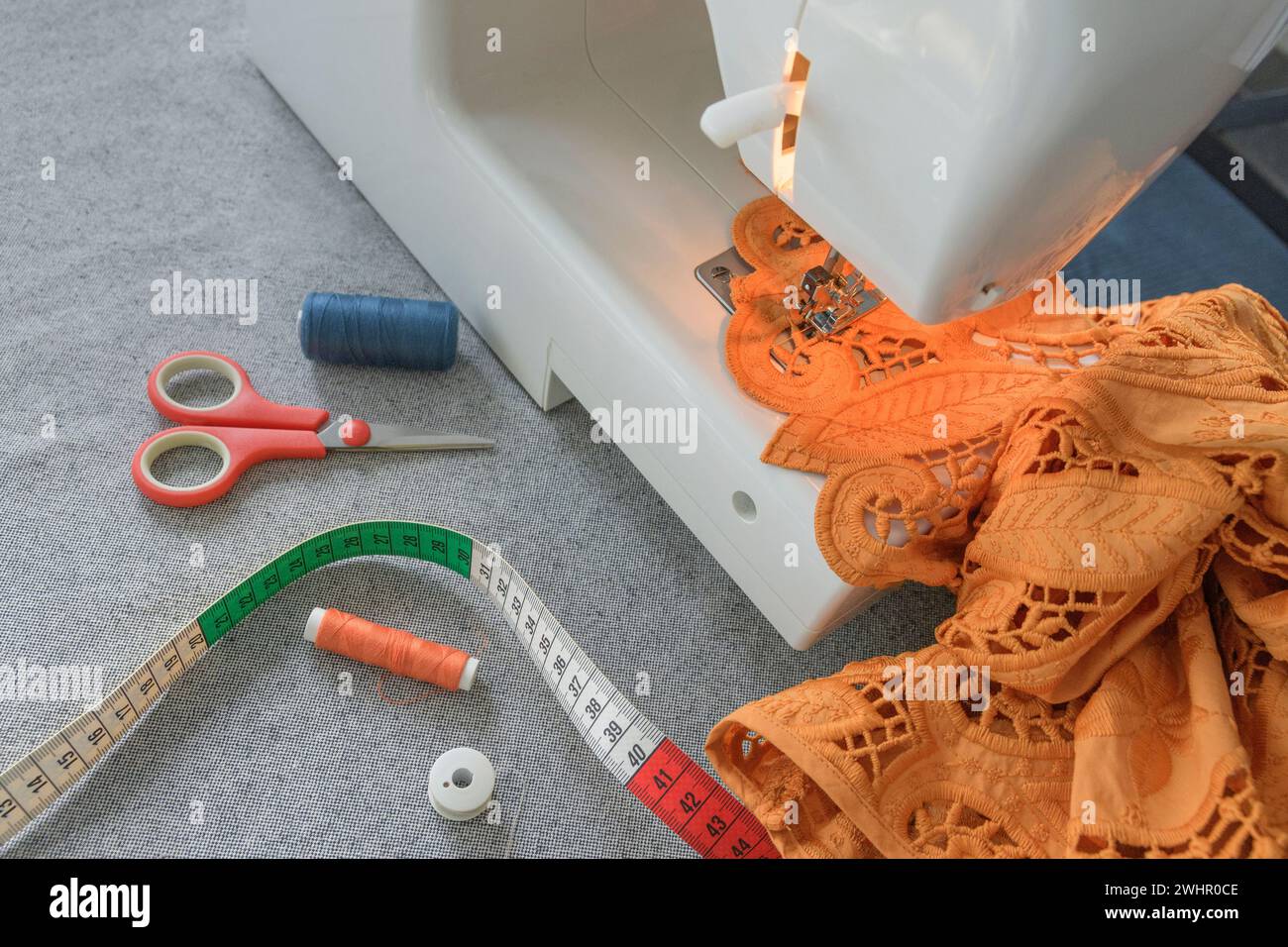 Gros plan d'une machine à coudre depuis le côté. Coudre un tissu orange ajouré avec de la dentelle sur une machine à coudre domestique. Banque D'Images