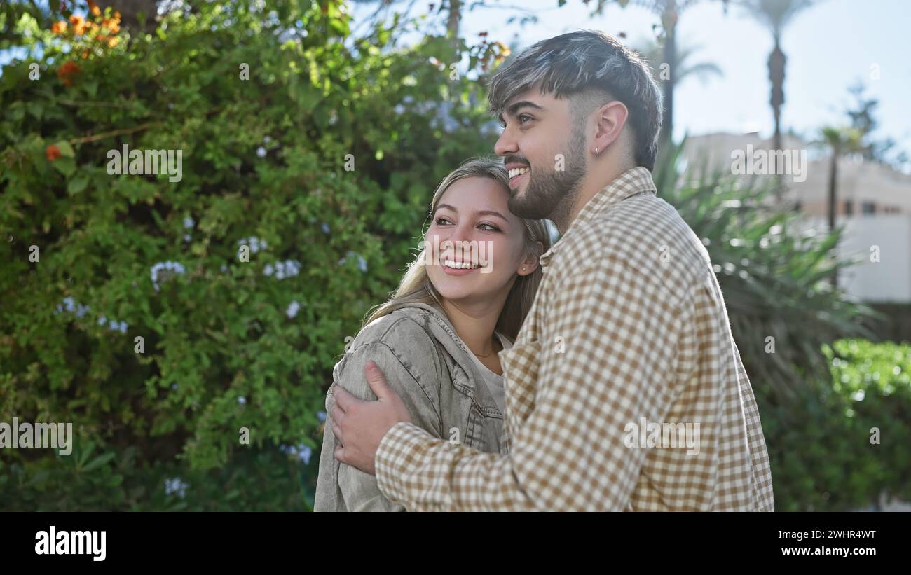 Une femme et un homme souriants s'embrassent joyeusement dans un jardin luxuriant, mettant en valeur l'amour et la compagnie dans un cadre naturel en plein air. Banque D'Images