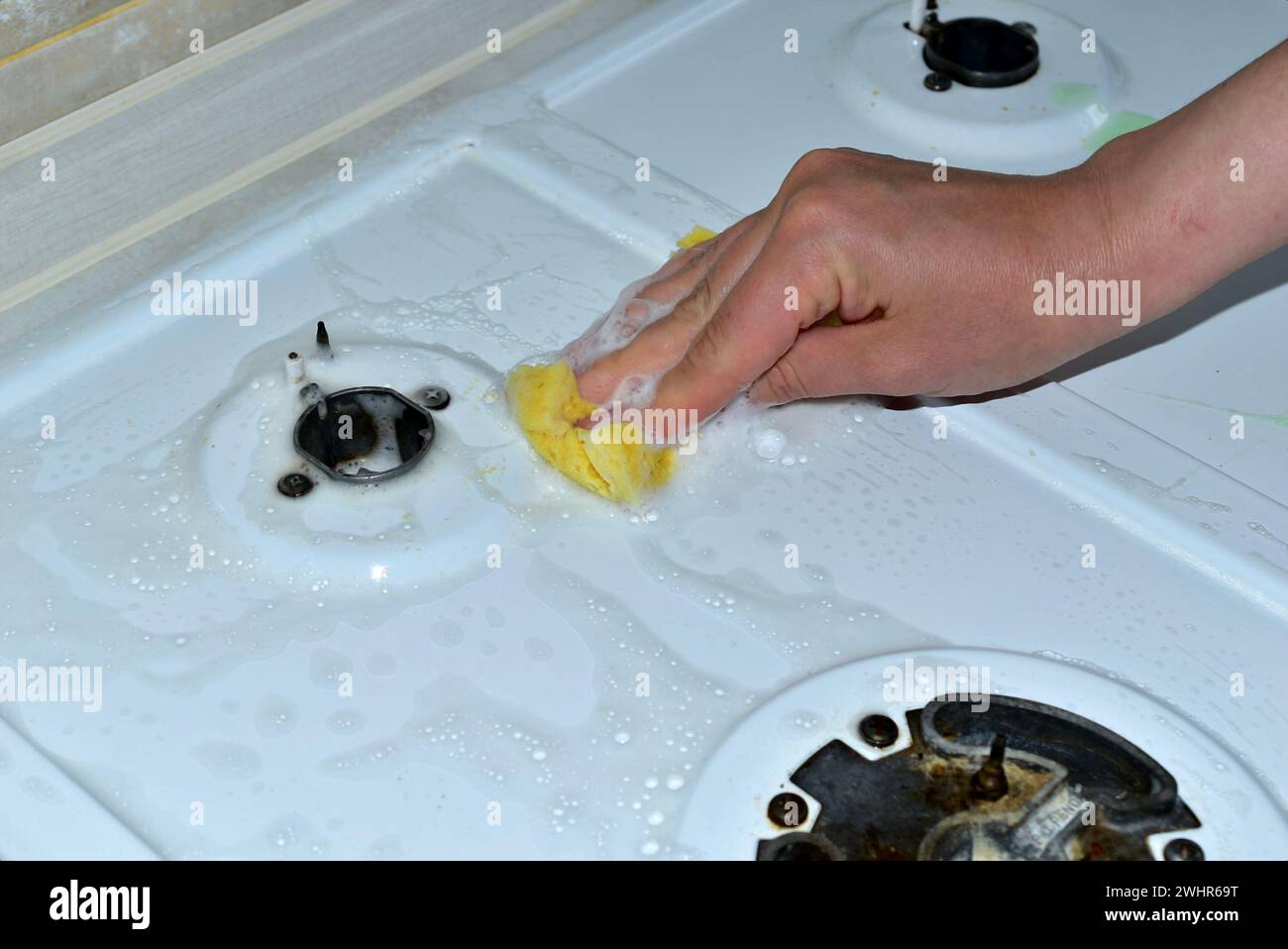 Sur l'image, une femme lave la surface d'une cuisinière à gaz avec une éponge et des détergents. Banque D'Images
