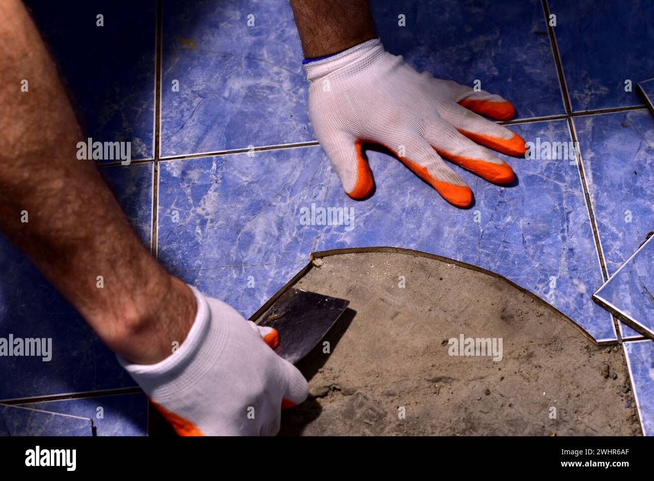 Sur la photo, les mains des hommes habillées de mitaines avec une spatule sont engagées dans les réparations du sol en céramique. Banque D'Images