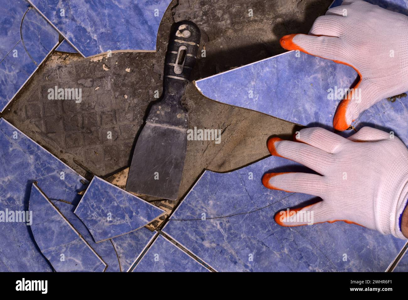 Le maître avec une spatule arrache les carreaux de céramique fissurés du sol. Banque D'Images