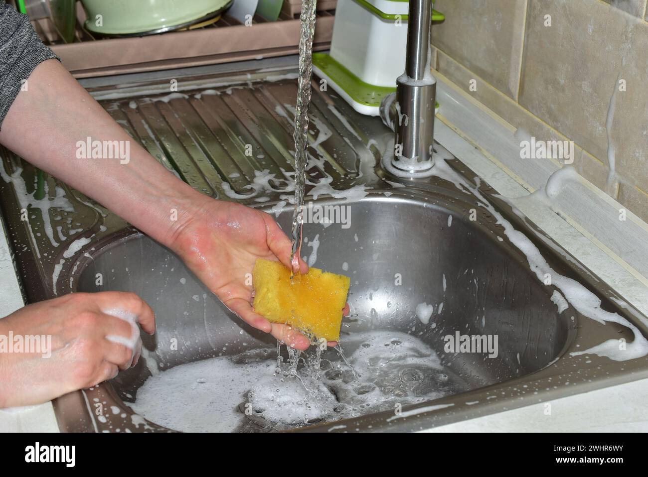 Sur l'image, la main d'une femme lave un gant de toilette sur l'évier sous l'eau courante. Banque D'Images