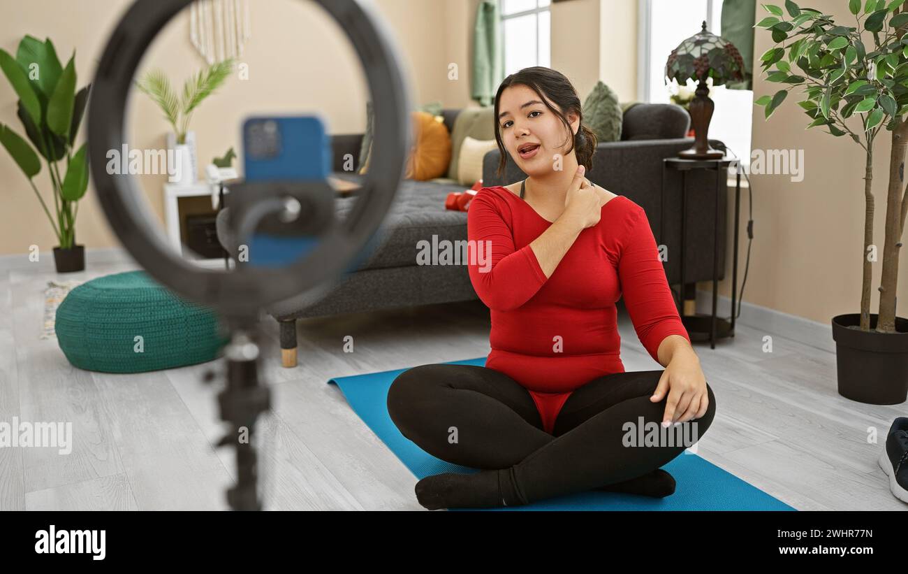 Une jeune femme hispanique dans un haut rouge enregistre un vlog chez elle, créant du contenu attrayant pour ses abonnés. Banque D'Images
