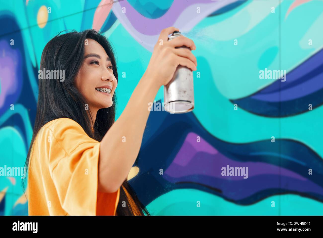 Artiste de rue féminine souriante peignant des graffitis colorés sur le mur Banque D'Images