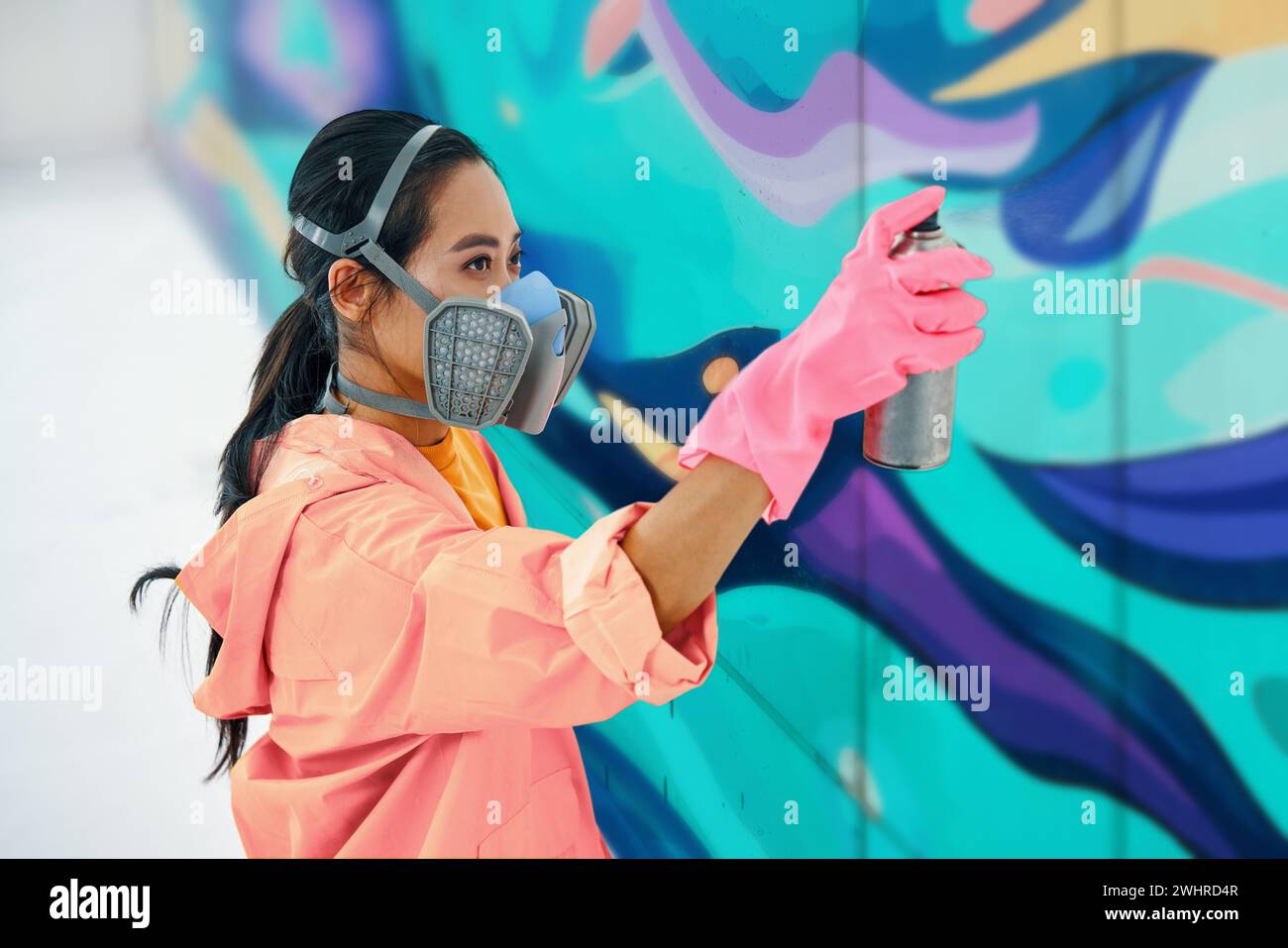Peintre de rue féminine dans le masque respiratoire peignant graffiti coloré sur le mur Banque D'Images