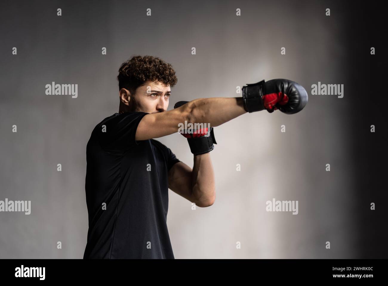 Homme avec des gants de boxe rouges de formation sur un sac de punching dans le gymnase Banque D'Images