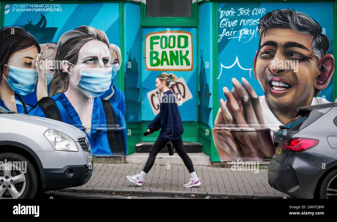 Une jeune femme passant devant un magasin à Bedminster Bristol Royaume-Uni a peint comme une banque alimentaire avec des infirmières faisant la queue dans la campagne Don't Just Clap pour une rémunération équitable des infirmières Banque D'Images