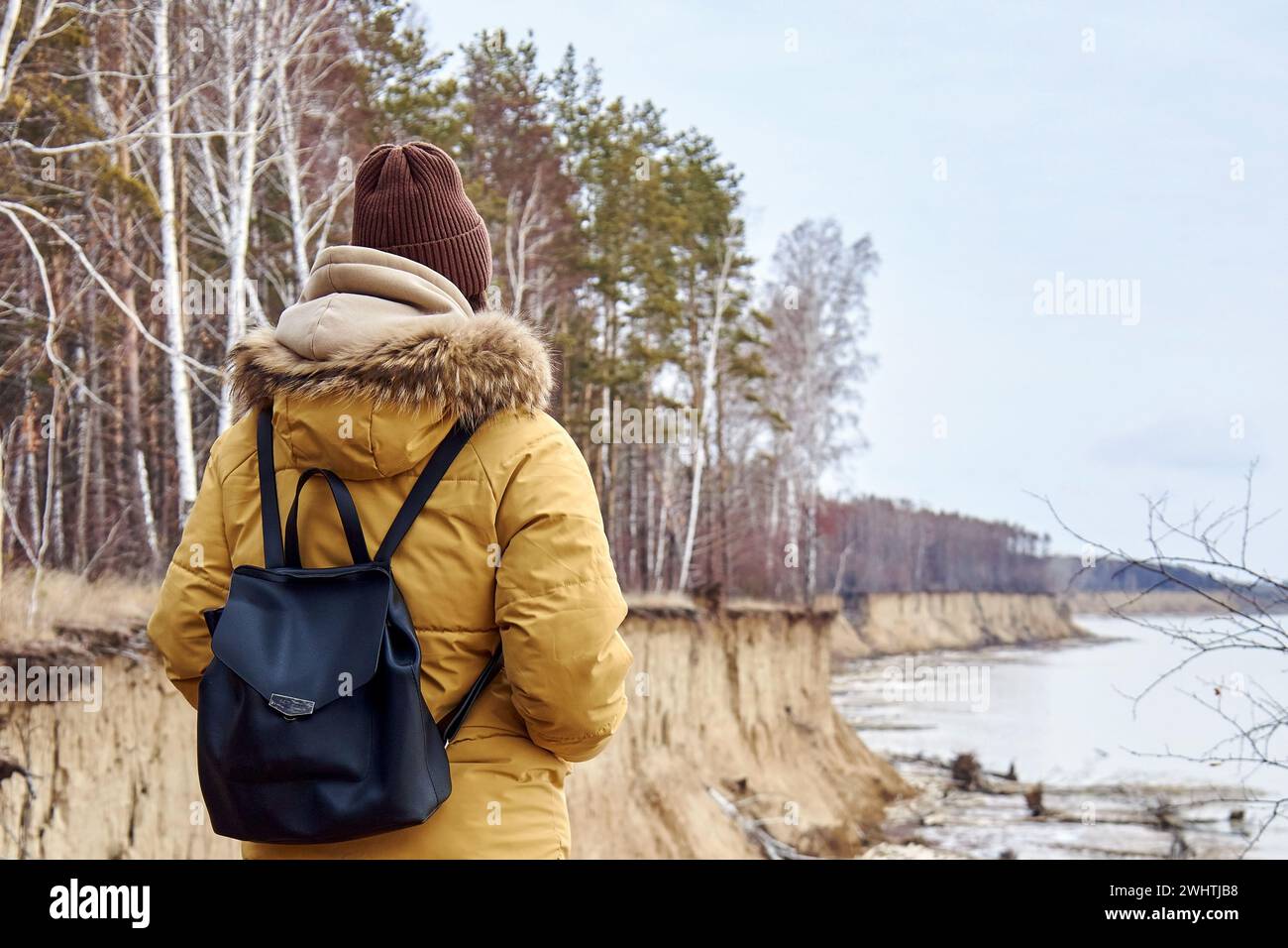 Femme en veste de couleur sable, chapeau brun et sac à dos de ville noir se tient derrière la caméra, regarde l'étang et la rive de la falaise. Côte de mer d'hiver, hors saison, Banque D'Images