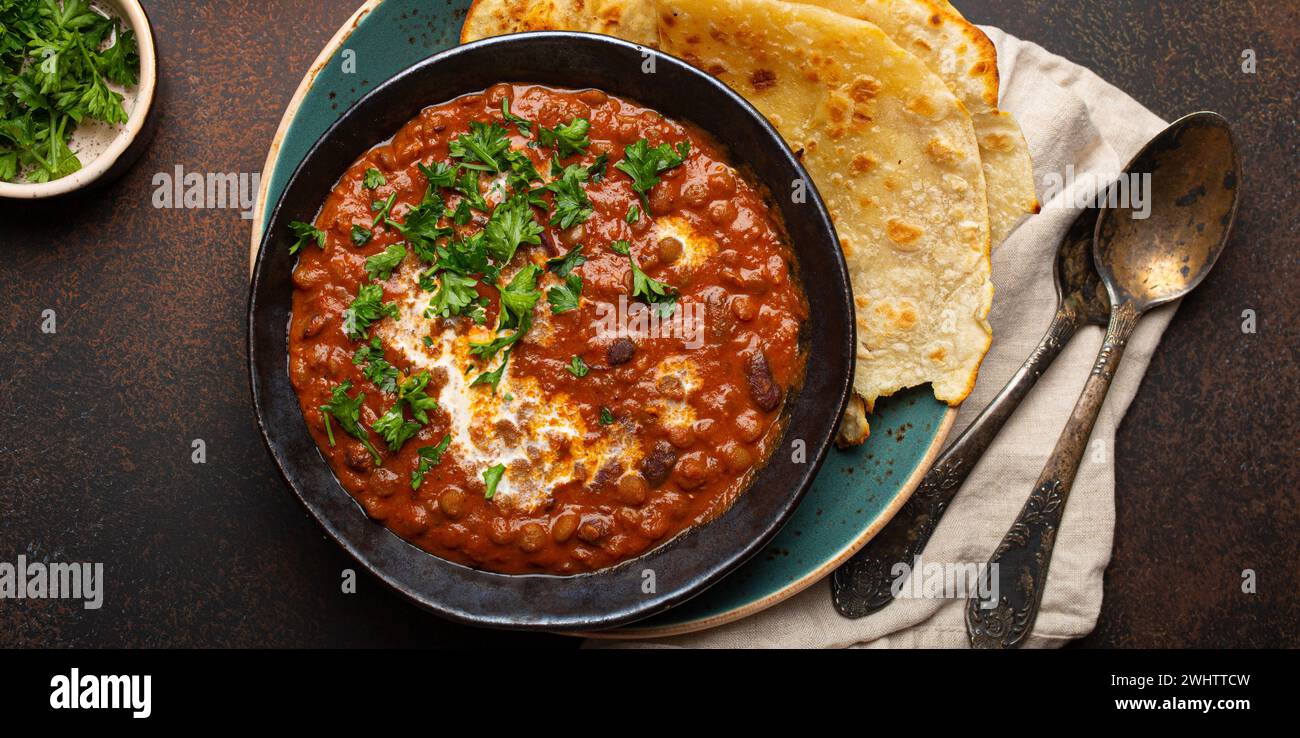 Plat traditionnel indien pendjabi Dal makhani avec lentilles et haricots dans un bol noir servi avec du pain plat naan, coriandre fraîche et Banque D'Images