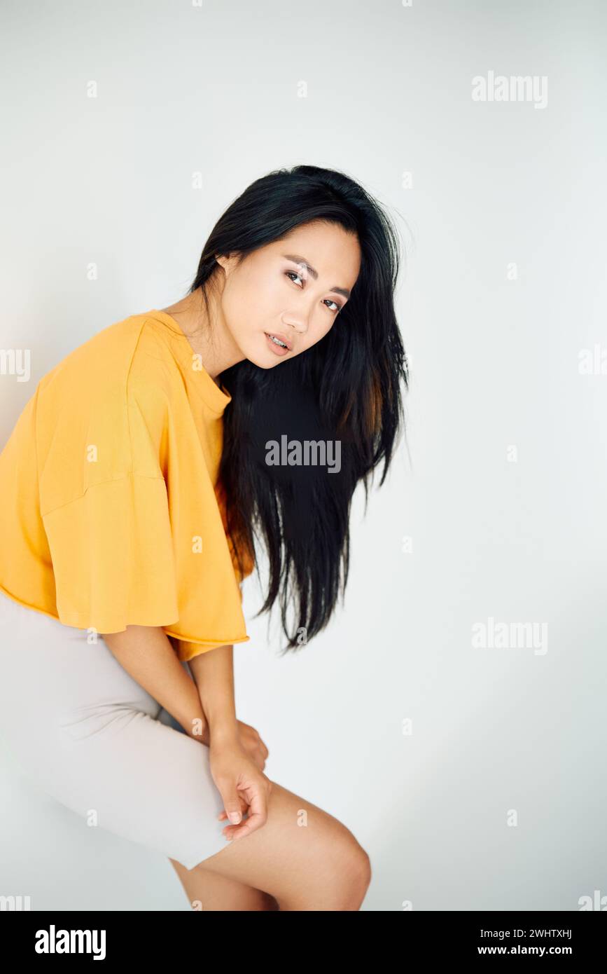 Jolie jeune femme asiatique en t-shirt jaune vif posant sur fond blanc de studio Banque D'Images