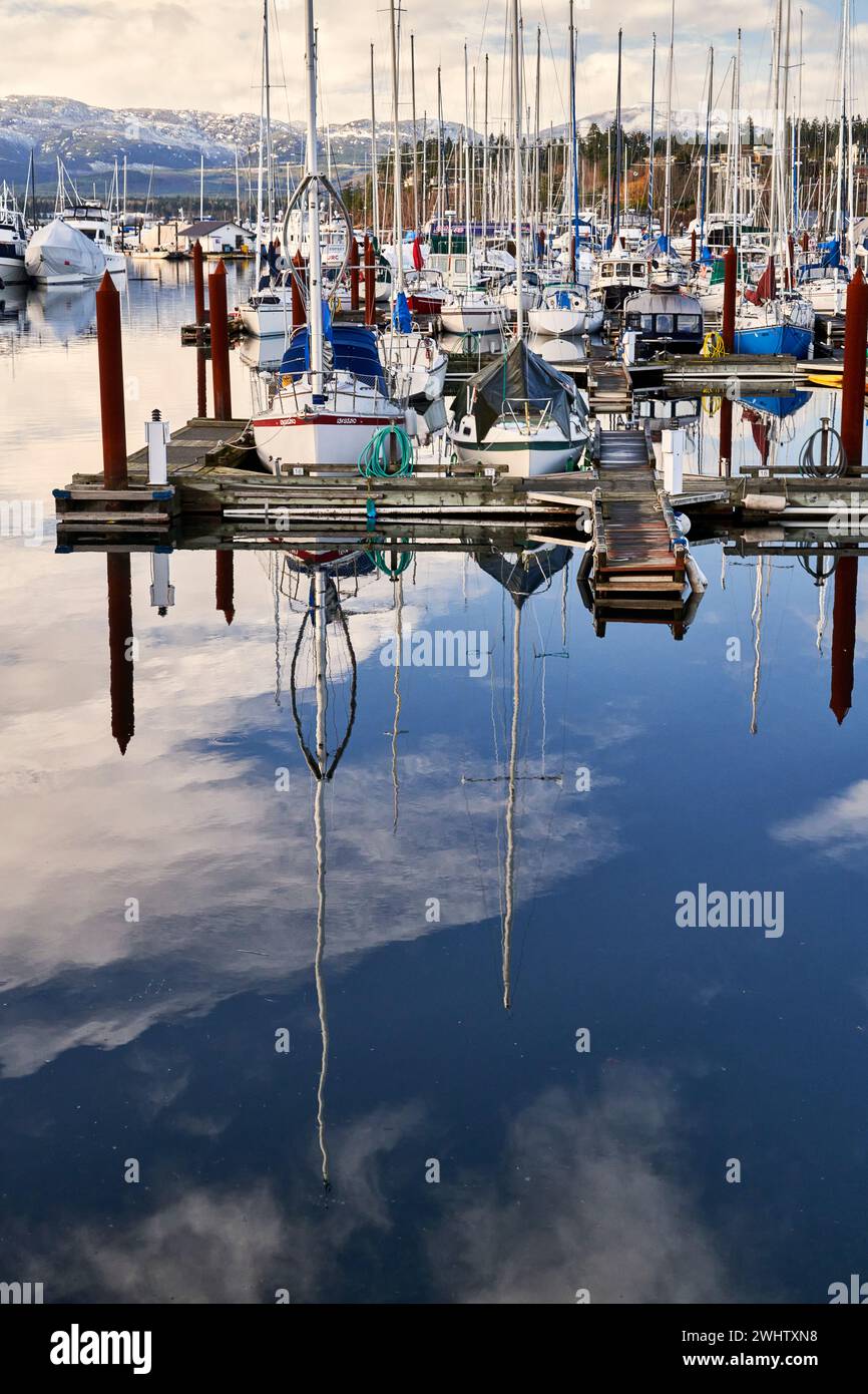 Voiliers et bateaux à moteur attachés à la marina du port de Comox avec la passerelle menant à des montagnes recouvertes de neige lointaines Banque D'Images