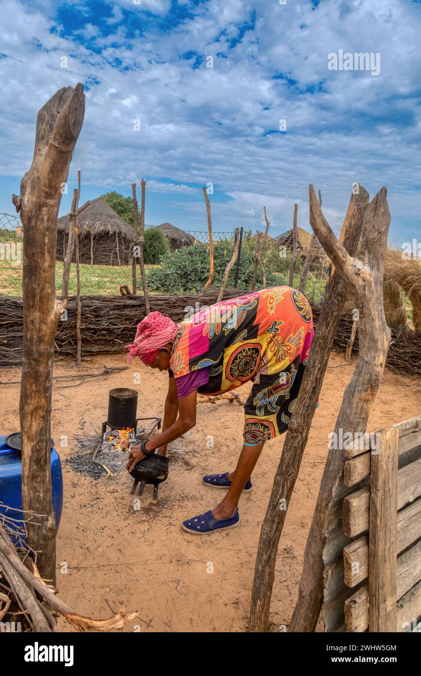 village vieille femme africaine cuisinant dans la cuisine extérieure et lavant un pot à trois pattes Banque D'Images