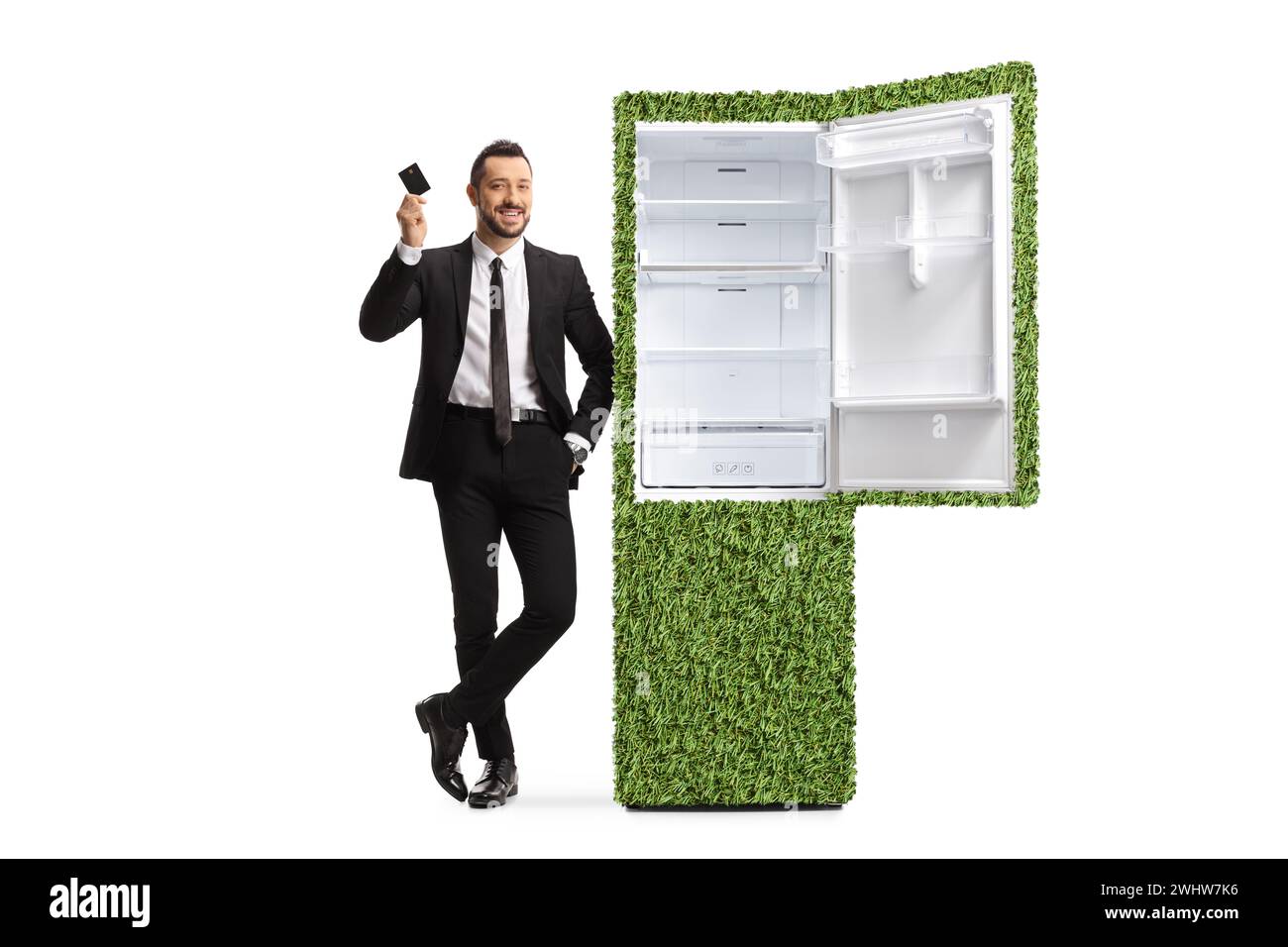 Homme d'affaires dans un costume appuyé sur un réfrigérateur économe en énergie et tenant une carte de crédit isolé sur fond blanc Banque D'Images