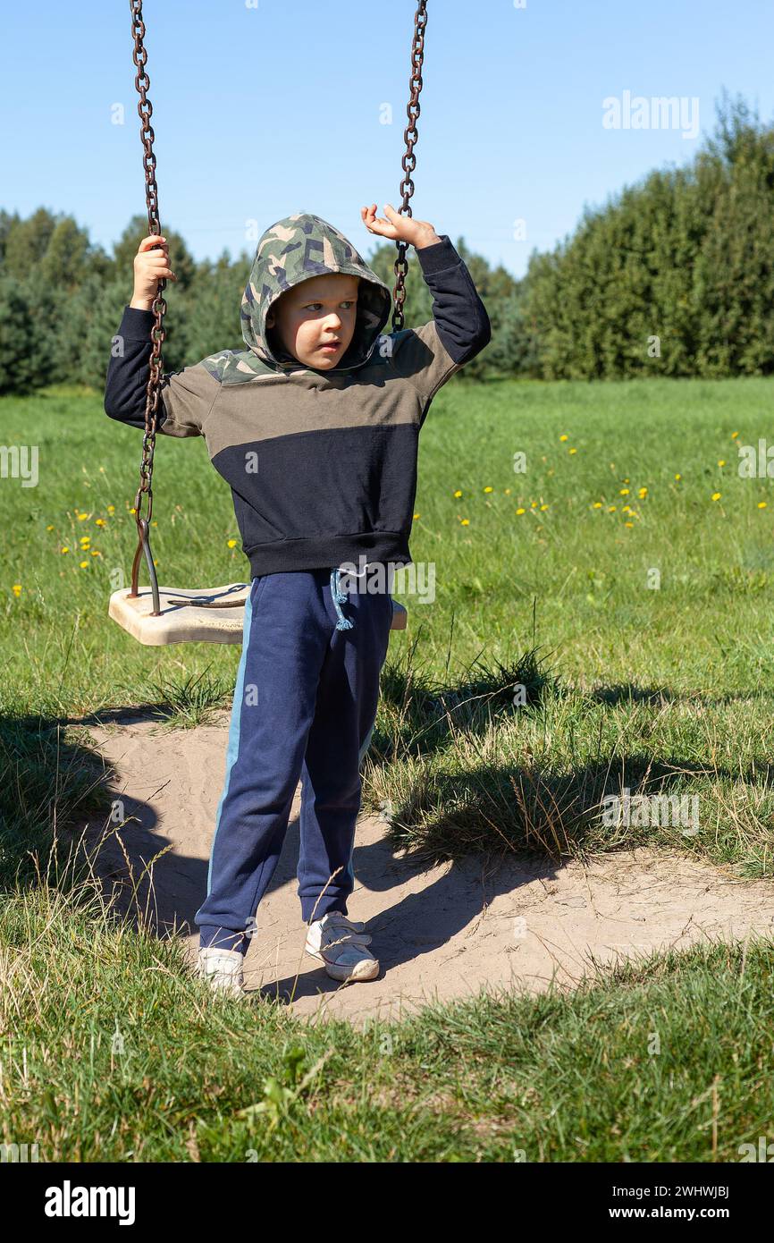 Petit garçon s'amusant sur une balançoire sur le terrain de jeu dans le parc public le jour d'été. Un enfant heureux se balancer. Activités de loisirs en plein air pour les enfants en ville Banque D'Images