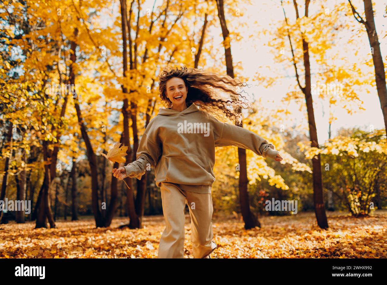 Jeune femme souriante joue et saute dansant dans la forêt d'automne avec les feuilles jaunes au coucher du soleil. Banque D'Images