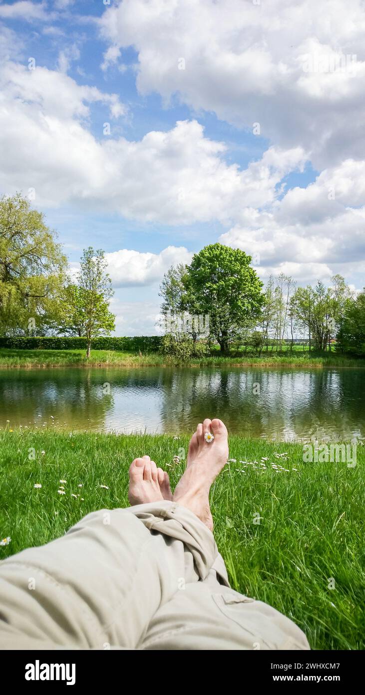 Les jambes et les pieds se détendre en face de l'étang de l'eau douce sereine Banque D'Images