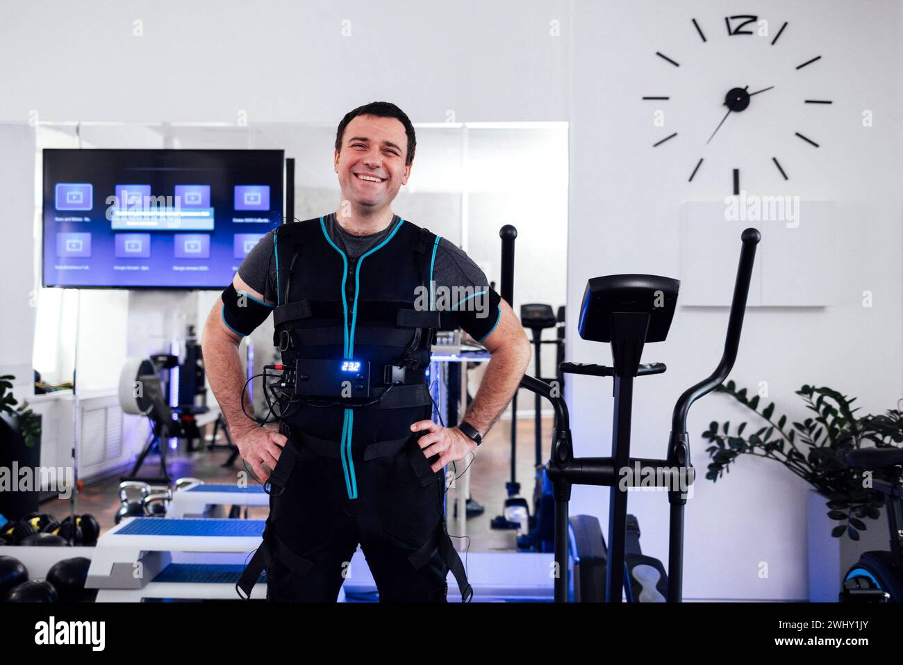 Portrait de l'homme souriant satisfait en costume spécial ems debout au milieu de la salle de gym ou club de fitness. Banque D'Images
