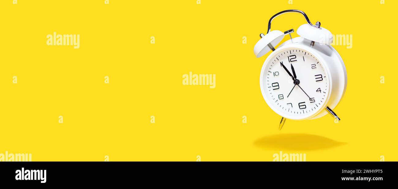 Réveil à cloche blanche planant sur fond jaune. concept d'horloge 5 à 12 isolé. Banque D'Images