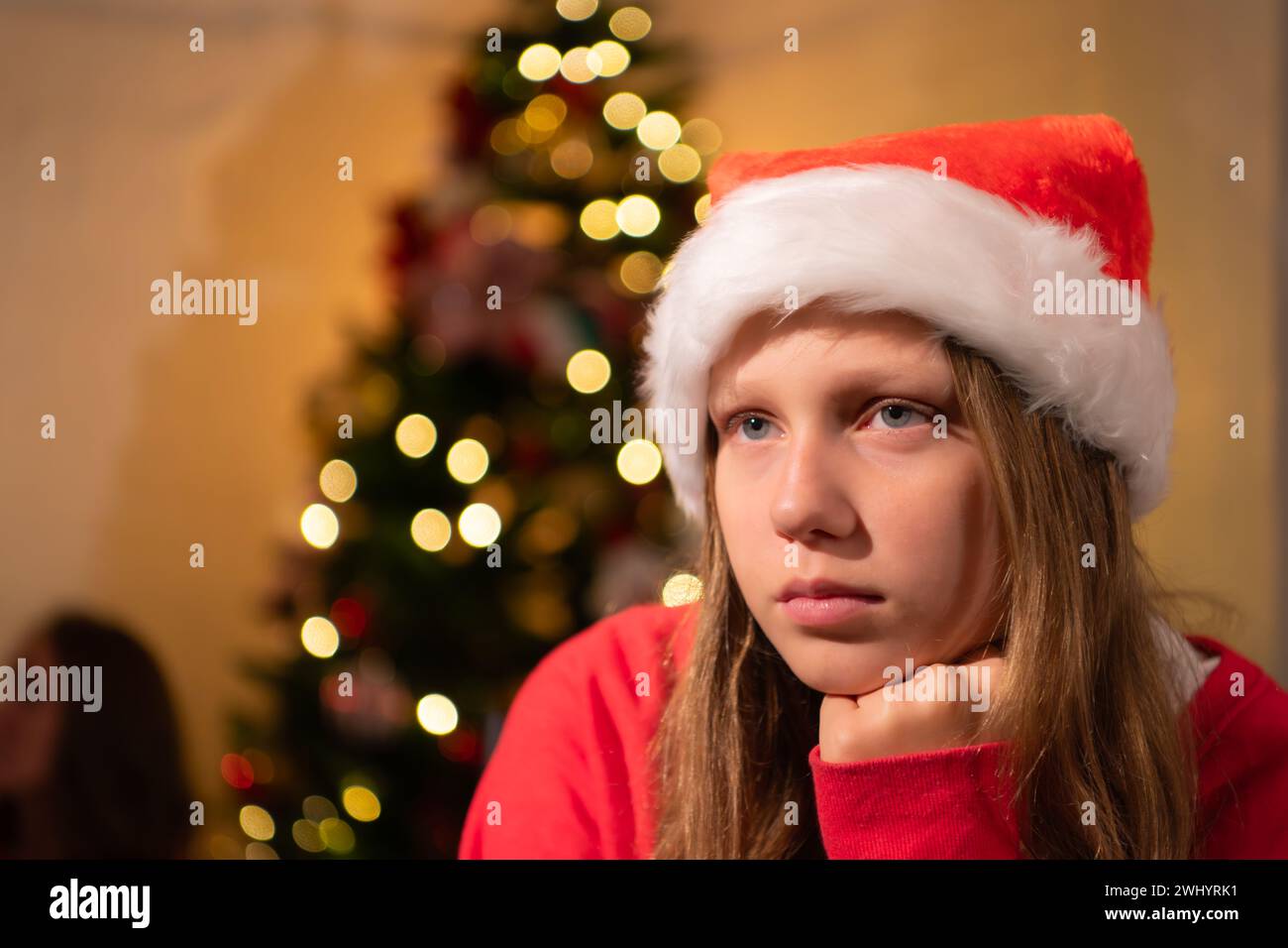 Portrait de l'adolescente dans le chapeau de Père Noël assis sur la chaise devant l'arbre de Noël, joyeux Noël et joyeuses fêtes! Banque D'Images