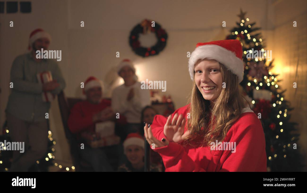 Portrait de l'adolescente dans le chapeau de Père Noël assis sur la chaise devant l'arbre de Noël, joyeux Noël et joyeuses fêtes! Banque D'Images