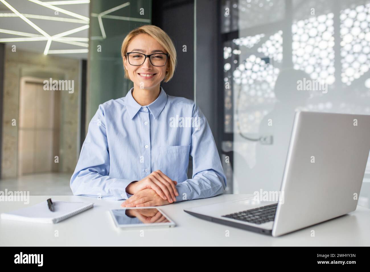 Femme satisfaite avec une coupe de cheveux courte pliant les mains sur le bureau avec ordinateur et cahier avec stylo. Le responsable des RH souriant se prépare à l'entrevue et accueille le nouveau candidat pour un poste dans l'entreprise Banque D'Images