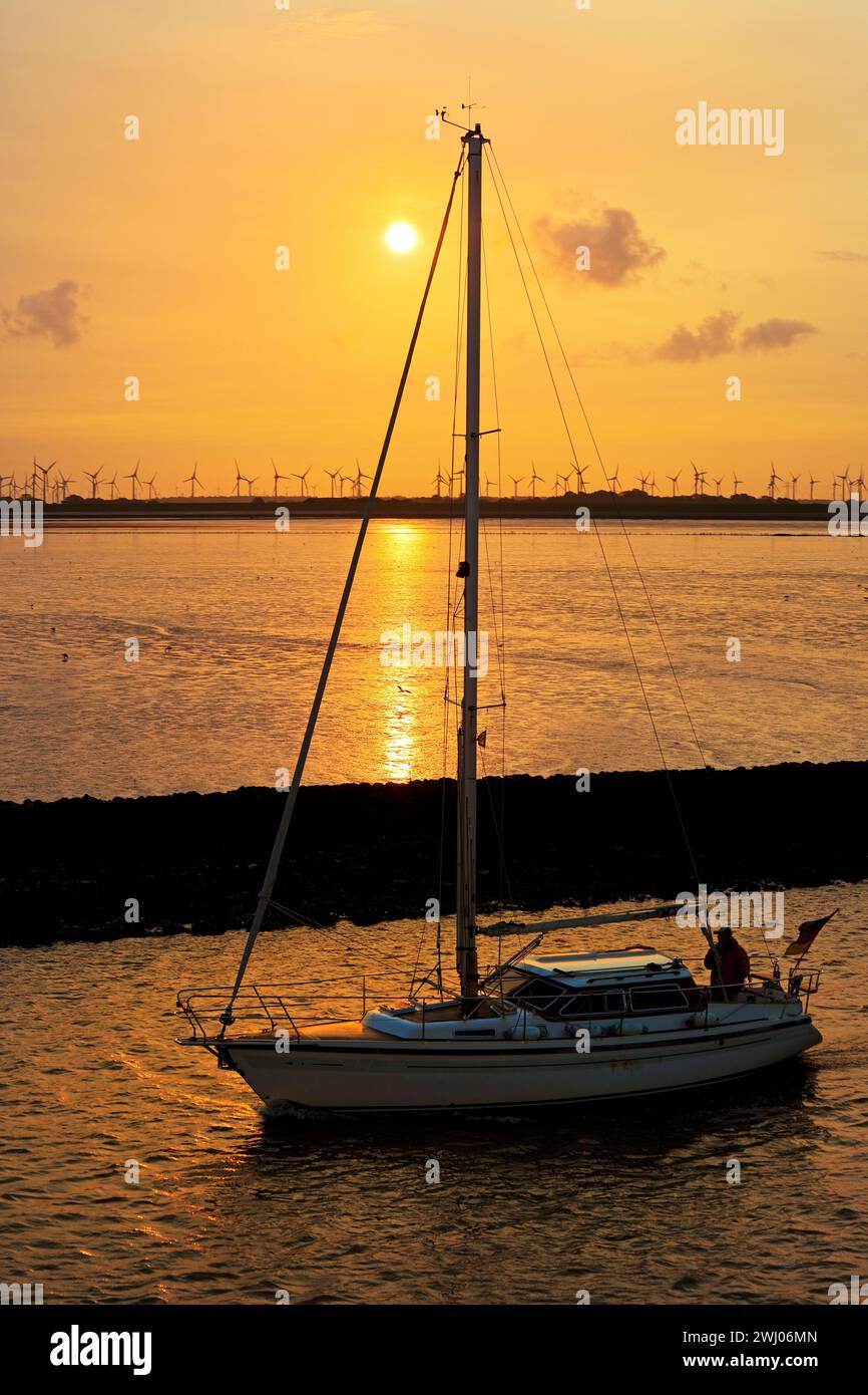 Voilier sur la mer du Nord au lever du soleil devant les vasières et les éoliennes, Norddeich, Allemagne Banque D'Images
