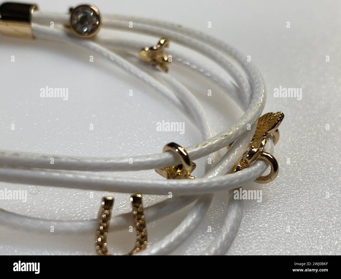 Trois bracelets en cordon blanc avec fermoirs et chaîne dorés Banque D'Images