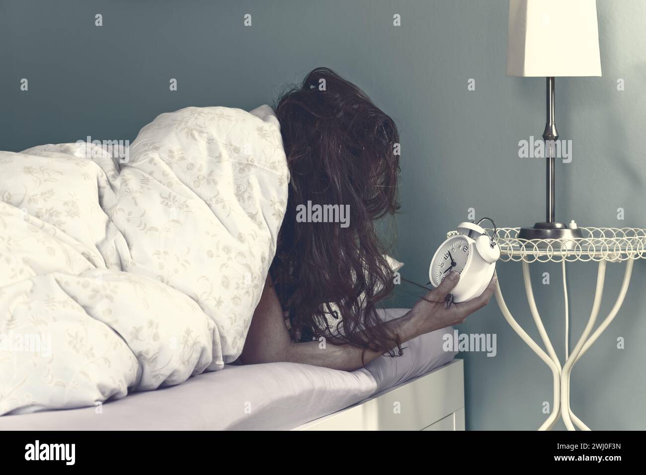 Femme se réveille sur le lit en regardant le réveil. Mettre le réveil dans la chambre à la maison Banque D'Images