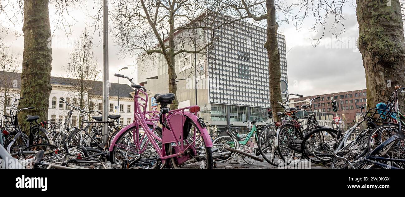 Parking chaotique de vélos design néerlandais sur le trottoir avec le lieu de divertissement musical Vredenburg en arrière-plan Banque D'Images