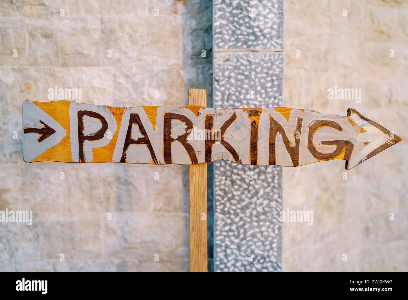 Pointeur en bois avec une flèche près du mur de pierre. Légende : parking Banque D'Images