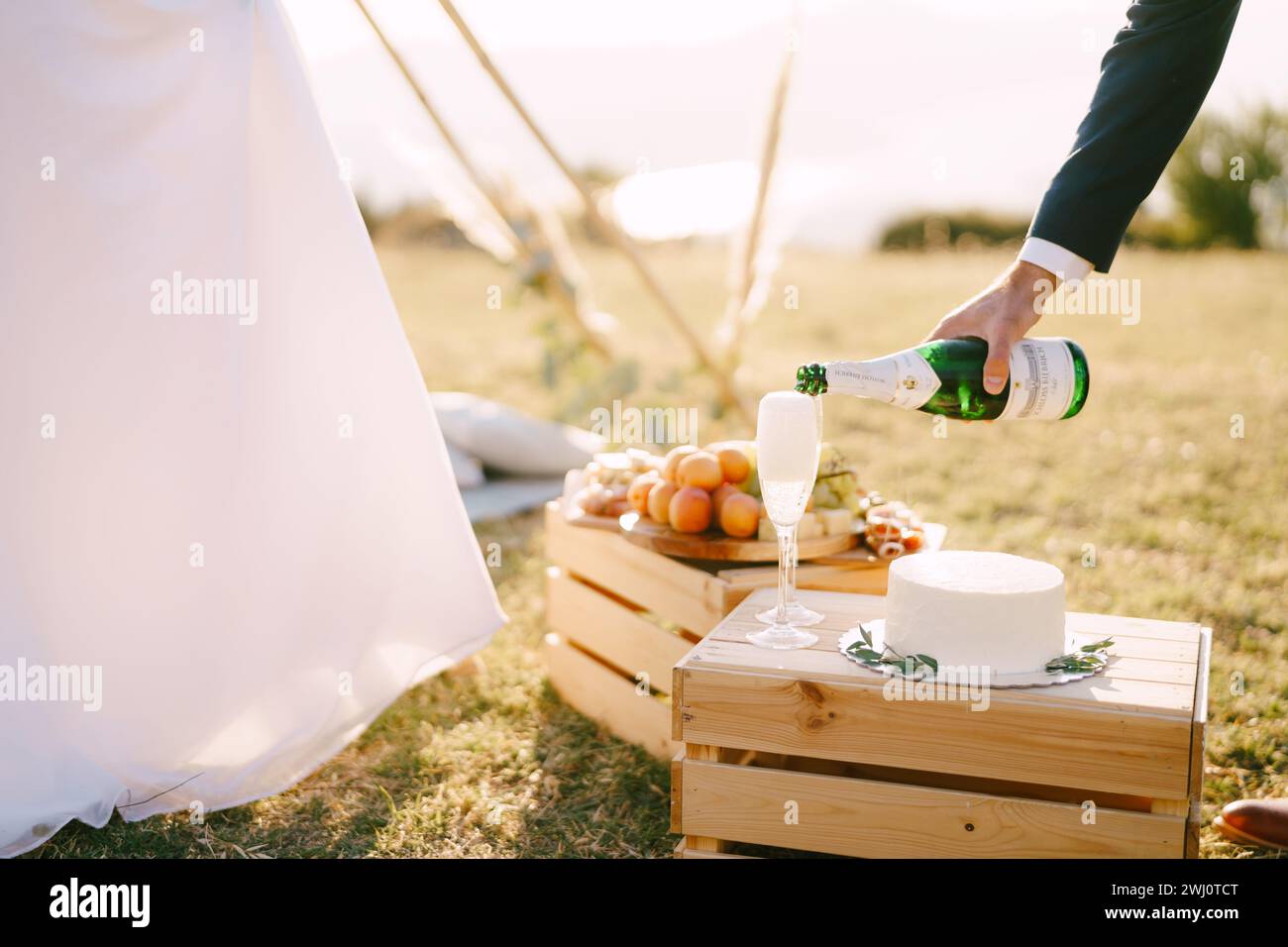 Le marié verse le champagne dans des verres sur une boîte en bois avec un gâteau à côté de la mariée. Rogné Banque D'Images