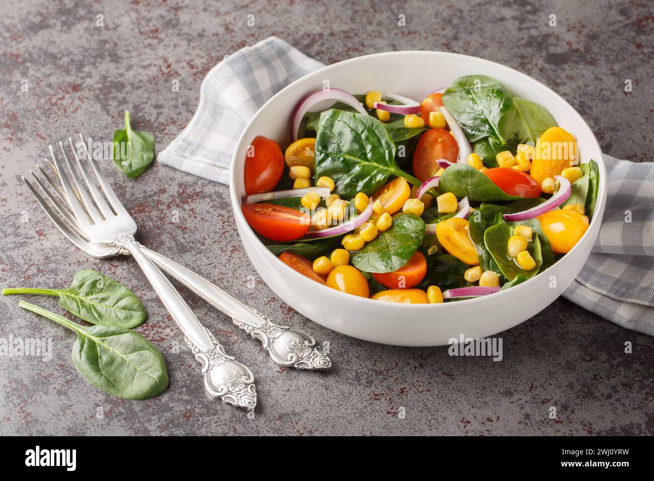 Salade végétarienne diététique de bébés épinards, maïs, tomates cerises et oignons vêtus d'huile d'olive gros plan dans un bol sur la table. Horizontal Banque D'Images